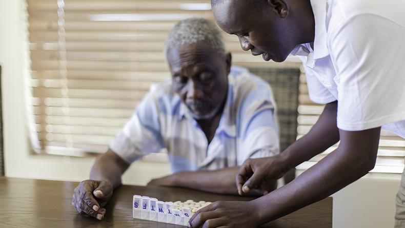 Caregiver assisting older gentleman with his daily pill container