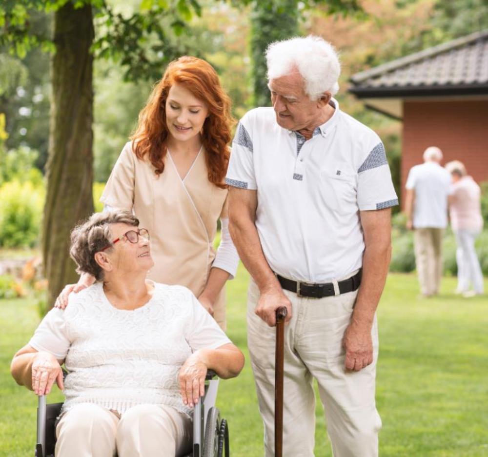 Older woman in wheelchair being pushed by young woman visiting with older man with cane in outside setting